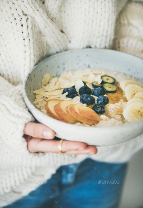 Woman in jeans and sweater holding bowl of oatmeal porriage - Stock Photo - Images