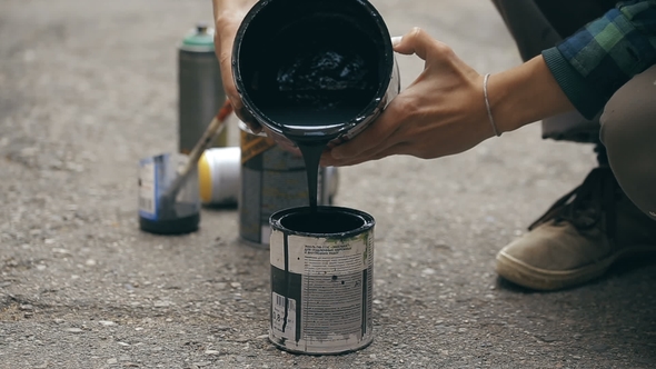 Artist Pouring a Black Paint From Can To Another Can.