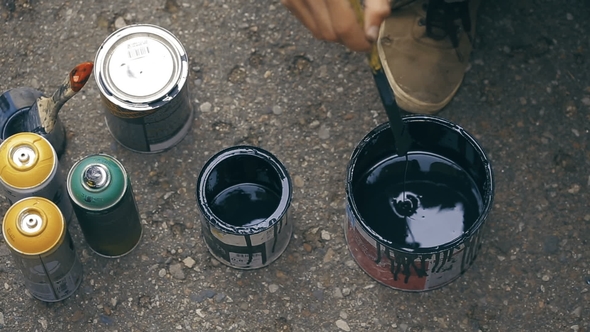 Artist Stir a Black Paint Into a Can and Pouring It To Another Can.