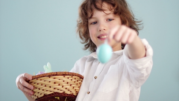 Boy with Easter Basket. Teenager Shows on His Outstretched Hand a Gently Blue Easter Egg alt