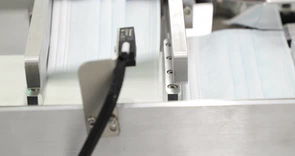 3-Ply Surgical Face Mask Coming Out Of Machine To Ear Loop Attaching. close up, panning right alt