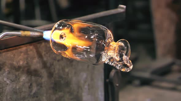 Glass artist rotates vase while heating it with blowtorch. Close up. alt