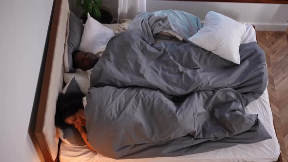 High Angle View Portrait of Sleepless African American Wife Covering Ears with Hands As Husband alt