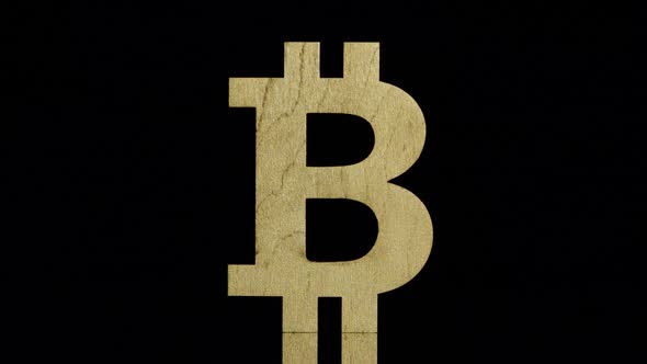 Golden bitcoin symbol stands and falls back on a black background