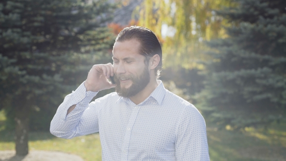 Handsome Man Makes a Call and Softly Talks on the Smartphone with Smile alt
