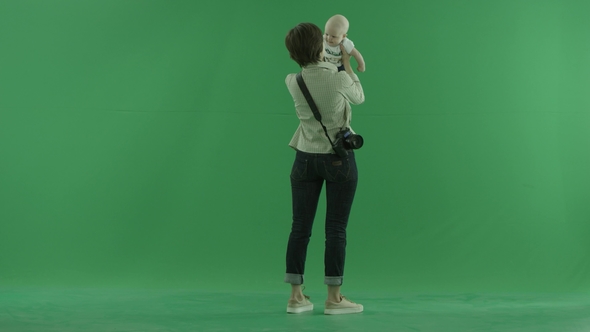 A Young Woman Lifts Her Baby on the Side Back To the Viewer on the Green Screen