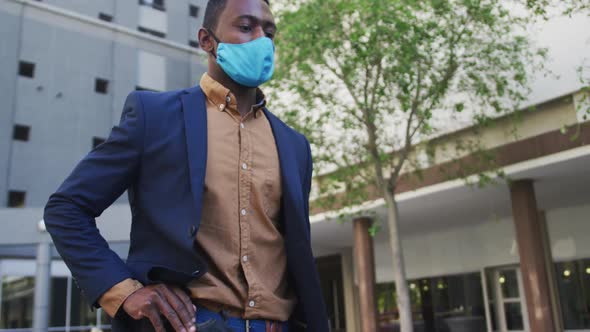 African american businessman wearing face mask using smartphone in street alt