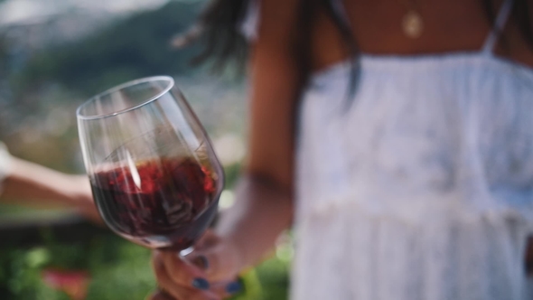 Hand of Young Woman Shakes Glass of Red Wine Outdoors