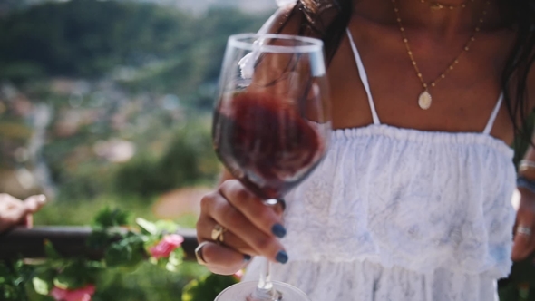Hand of Young Female Shakes Glass of Red Wine Outdoors