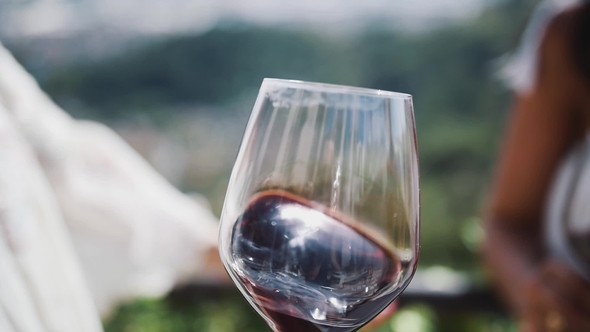 Hand of Adult Woman Shakes Glass of Red Wine Outdoors