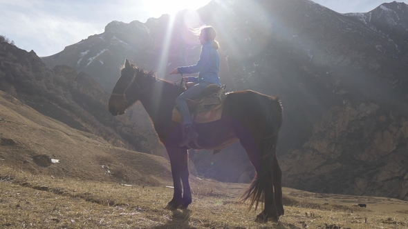 Young Beautiful Girl Riding a Horse in Back Lighting in the Mountains