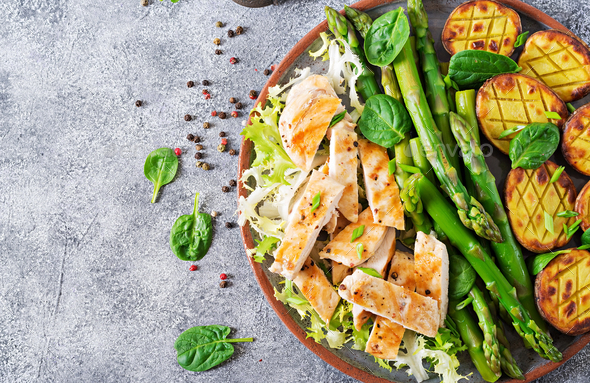 Chicken fillet cooked on a grill with a garnish of asparagus and baked potatoes. - Stock Photo - Images
