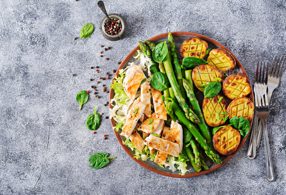 Chicken fillet cooked on a grill with a garnish of asparagus and baked potatoes. - Stock Photo - Images