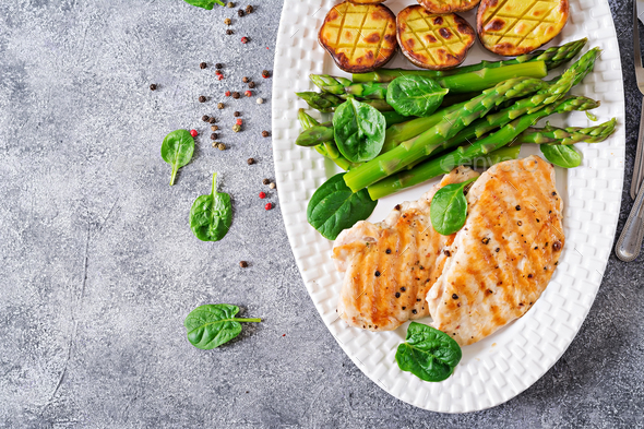 Chicken fillet cooked on a grill with a garnish of asparagus and baked potatoes. - Stock Photo - Images