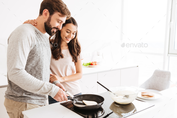 Portrait of a joyful young couple cooking pancakes Stock Photo by vadymvdrobot