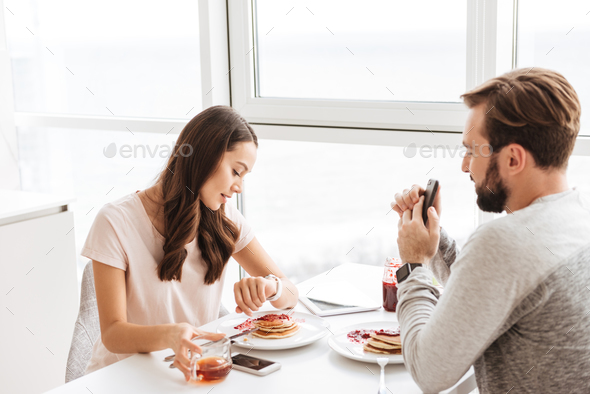 Pretty young couple having breakfast while sitting together - Stock Photo - Images