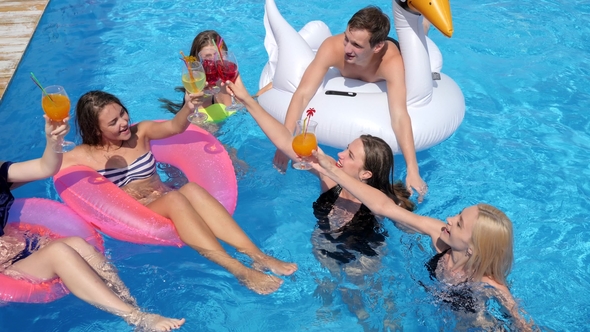 Company of Friends on Inflatable Rings with Cocktails in Hands Having Fun in Pool