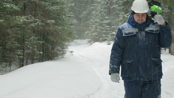 Worker With Chain Saw Going Through the Winter Forest