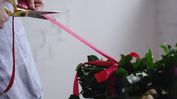 Florist Cuts the Red Ribbon on the Bouquet with Scissors