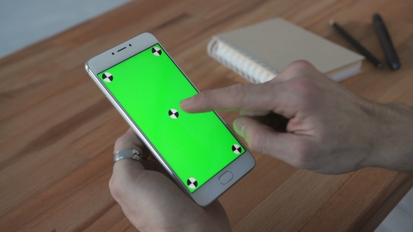 Man Using Phone with Green Screen Display at Desk alt