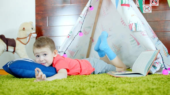 Little Boy Is Reading Book in His Self Made Wigwam in Playroom alt