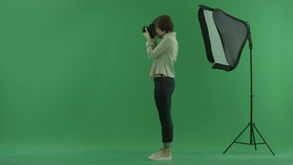 A Young Woman Taking Photos on the Left Hand Side on the Green Screen and Corrects Standing of a