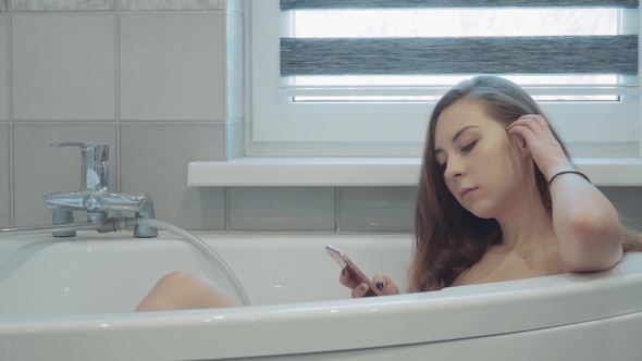 Pretty Young Woman Wathing in Cellphone in Bathroom