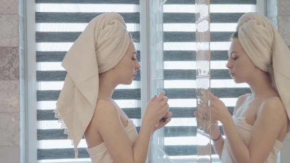 Beautiful Woman with Towel in Head and Body Applying Skincare Cream To Face Caring for Skin. Beauty