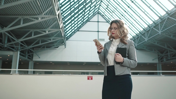 Portrait of a Business Woman Using a Smartphone. Girl in Business Clothes in the Spacious Lobby of alt
