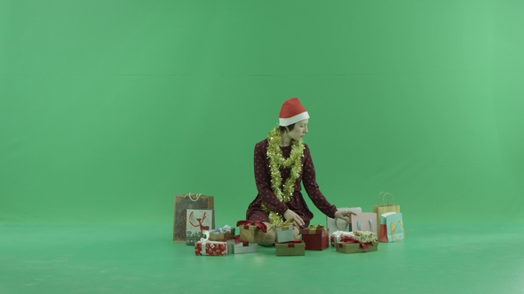 A Young Woman Is Sitting and Looking for a Christmas Gifts Near Her on the Green Screen