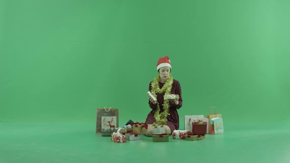 A Young Woman Is Sitting and Opening Empty Christmas Gifts Around Her on the Green Screen