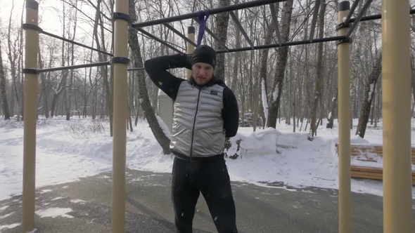 Athlete Man Doing Squat Exercise with Sport Expander on Winter Sports Ground alt