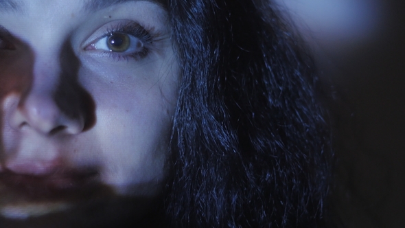 Portrait of a Young Woman Watching a Video or Film on TV or a Computer Monitor. Reflection on Her