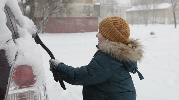 Little Boy Outdoors Cleaning a Snowy Car in Winter Morning