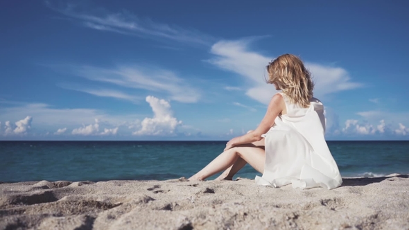A Girl Sits on the Sand and Sunbathes