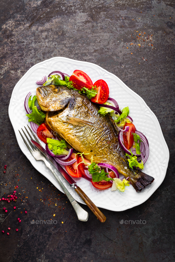 Baked fish dorado. Dorado fish oven baked and fresh vegetable salad on plate. Sea bream - Stock Photo - Images