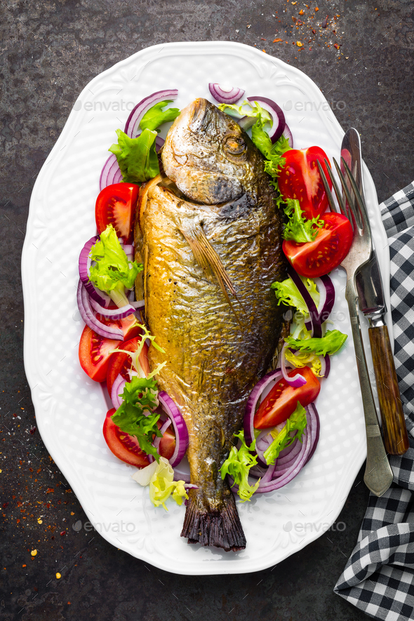 Baked fish dorado. Dorado fish oven baked and fresh vegetable salad on plate. Sea bream - Stock Photo - Images