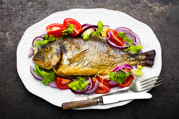 Baked fish dorado. Dorado fish oven baked and fresh vegetable salad on plate. Sea bream - Stock Photo - Images