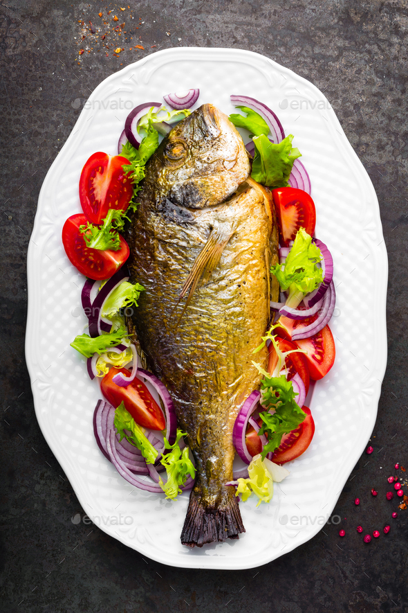 Baked fish dorado. Dorado fish oven baked and fresh vegetable salad on plate. Sea bream - Stock Photo - Images