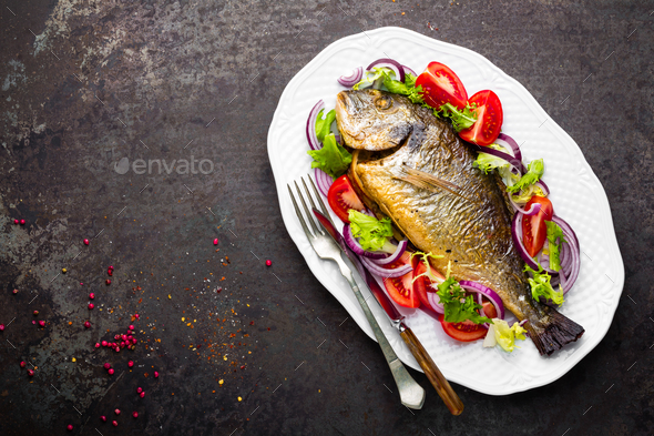 Baked fish dorado. Dorado fish oven baked and fresh vegetable salad on plate. Sea bream - Stock Photo - Images