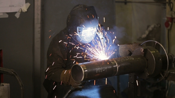 The Working Welder Processes the Metal, Prepares the Base A Man in a Protective Suit, Sparks. alt