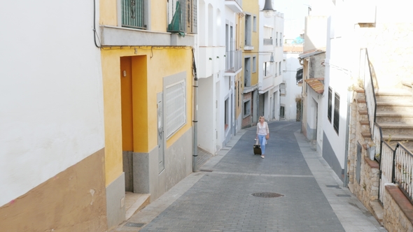 Tourist with Travel Bag Goes Up the Narrow Street of the Old European City in Spain alt