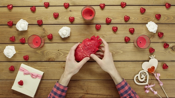 Man Looks at Plastic Human Heart By Wooden Table, Top View