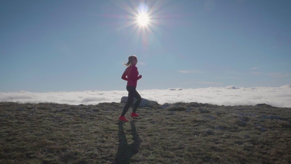 Young Woman Is Jogging in Mountains Above Clouds at Sunny Day. Sky Running alt