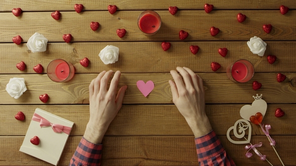 Young Man with Handmade Hearts of Paper Sits By Table, Top View
