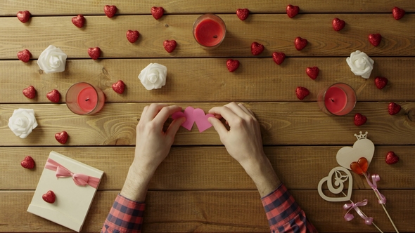 Young Man with Handmade Paper Hearts Sits By Wooden Table, Top View