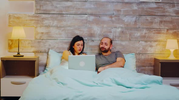 Young Couple in Pajamas Doing Shopping on Laptop alt