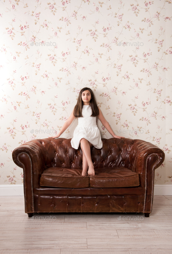 Portrait of a pretty little girl on a leather sofa - Stock Photo - Images
