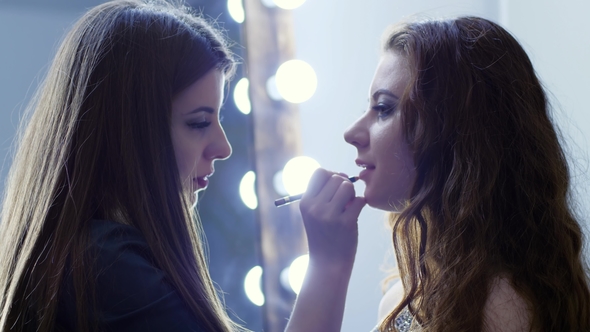 Visagiste Does Professional Make-up in Beauty Parlor on Background Lamps