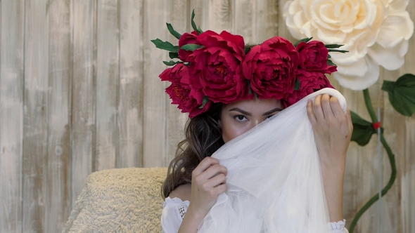 Girl Posing in Front of Camera. Young Woman in a Wreath of Scarlet Peonies on Her Head, Dark Long alt